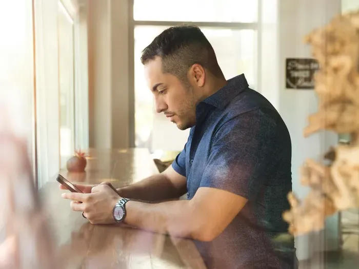 Man sitting by a bright cafe window, focused on smartphone while enjoying a relaxed moment